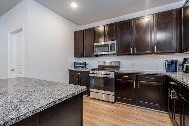 kitchen with light wood finished floors, appliances with stainless steel finishes, light stone counters, dark brown cabinets, and backsplash