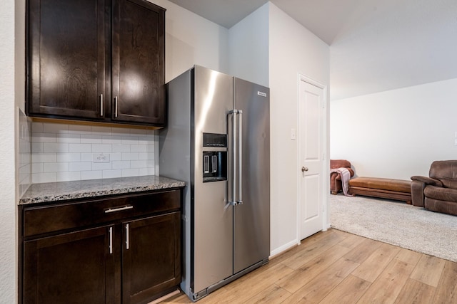 kitchen with open floor plan, high end fridge, light wood finished floors, and stone countertops