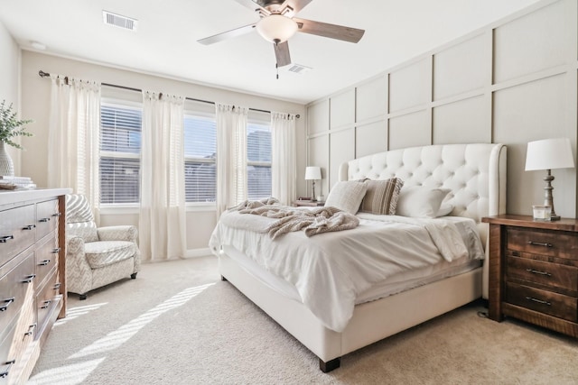 bedroom featuring ceiling fan, a decorative wall, visible vents, and light carpet