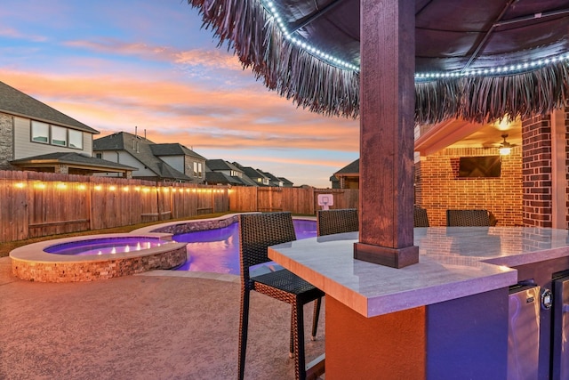 patio terrace at dusk with a fenced backyard, a pool with connected hot tub, and outdoor dry bar