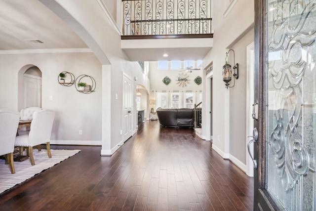 foyer entrance featuring baseboards, arched walkways, dark wood-type flooring, and a high ceiling