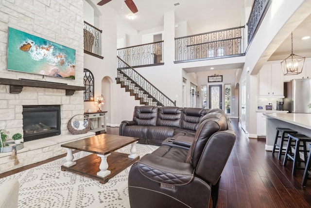 living room with stairway, baseboards, a fireplace, arched walkways, and dark wood-type flooring