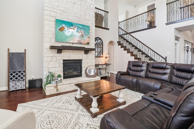 living room with wood finished floors, arched walkways, a stone fireplace, baseboards, and stairs