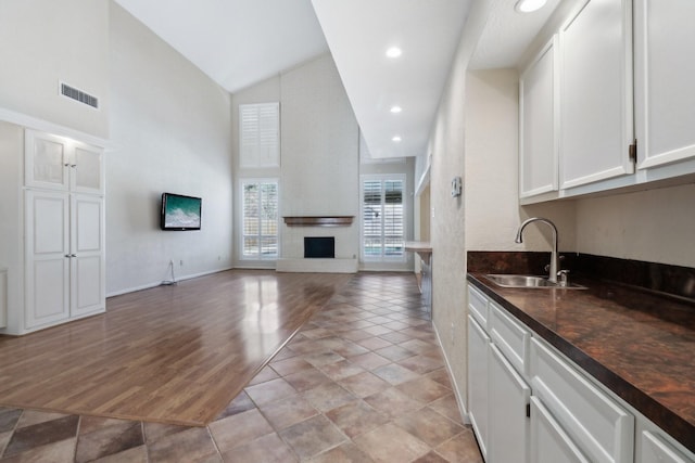 kitchen featuring dark countertops, visible vents, a large fireplace, white cabinets, and a sink