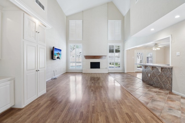 unfurnished living room with baseboards, visible vents, light wood-style floors, high vaulted ceiling, and a fireplace