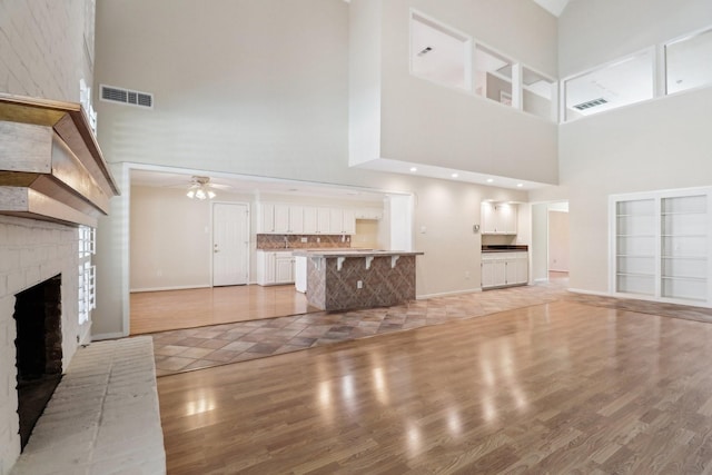 unfurnished living room featuring light wood-style flooring, visible vents, a towering ceiling, and a ceiling fan