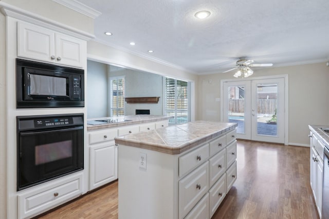 kitchen with crown molding, tile counters, light wood-style floors, white cabinetry, and black appliances