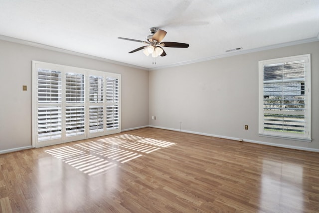 empty room featuring wood finished floors, visible vents, a ceiling fan, crown molding, and baseboards
