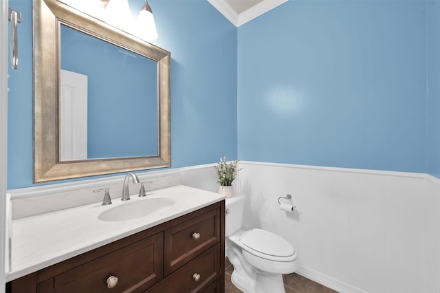 bathroom featuring wainscoting, crown molding, vanity, and toilet