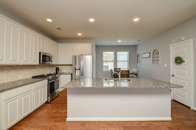 kitchen with wood finished floors, a sink, visible vents, appliances with stainless steel finishes, and an island with sink