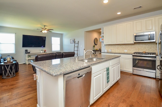 kitchen with dark wood finished floors, stainless steel appliances, visible vents, a kitchen island with sink, and a sink