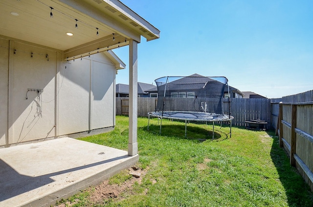 view of yard with a trampoline, a fenced backyard, and a patio