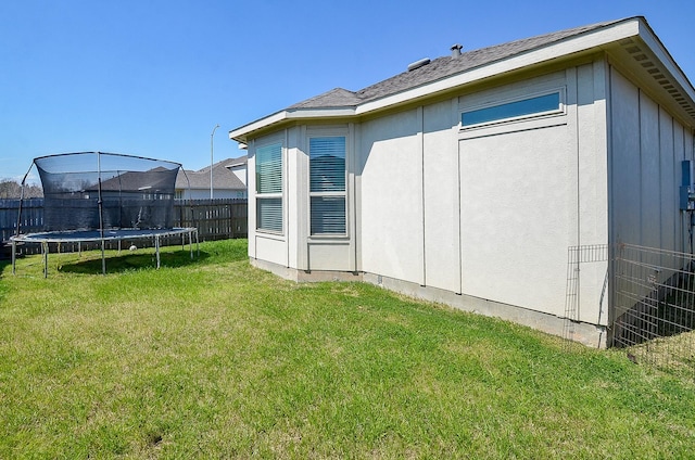 back of property featuring a trampoline, a lawn, and fence