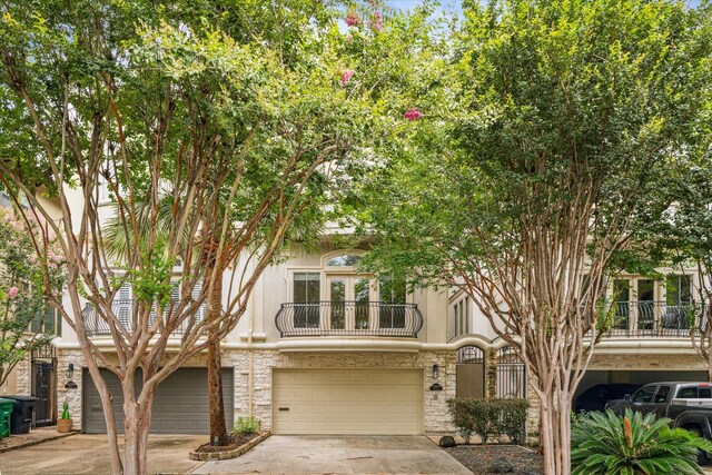 view of front of house with a balcony, driveway, an attached garage, stucco siding, and stone siding