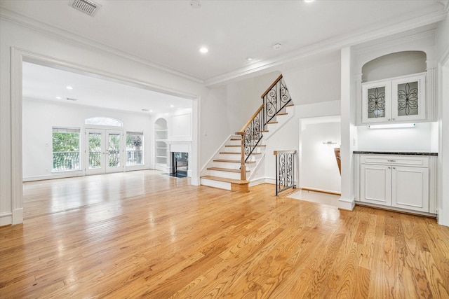 unfurnished living room with visible vents, a fireplace with flush hearth, stairs, light wood-type flooring, and ornamental molding