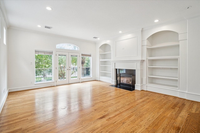 unfurnished living room with visible vents, built in shelves, a fireplace with flush hearth, crown molding, and light wood finished floors