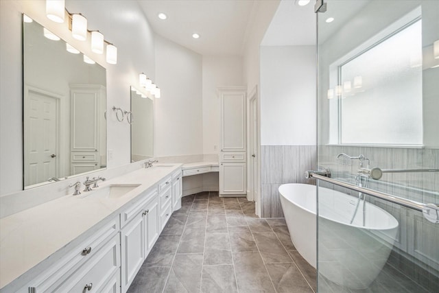 bathroom with double vanity, a freestanding tub, wainscoting, and a sink