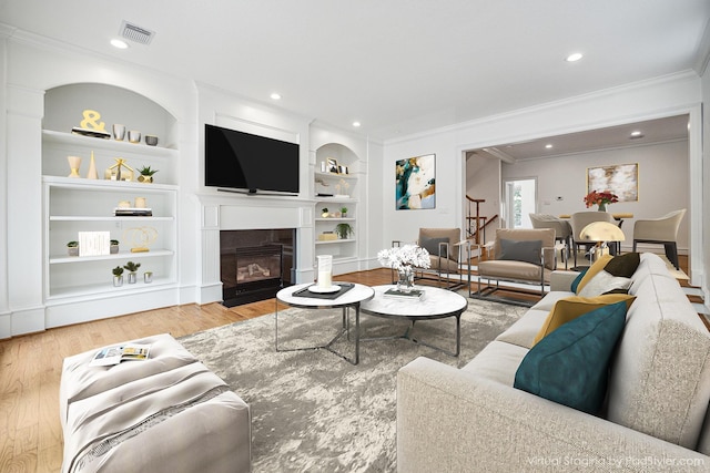 living area featuring visible vents, ornamental molding, built in features, a glass covered fireplace, and wood finished floors