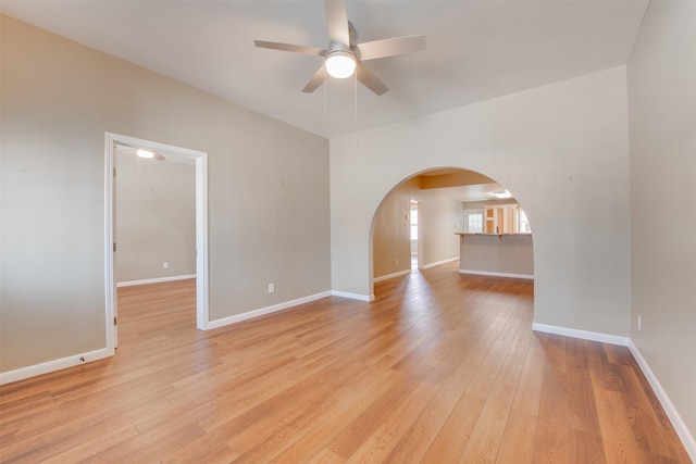 spare room featuring light wood-style floors, ceiling fan, arched walkways, and baseboards