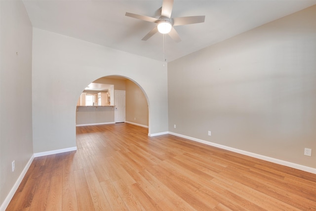 spare room featuring a ceiling fan, light wood-type flooring, arched walkways, and baseboards