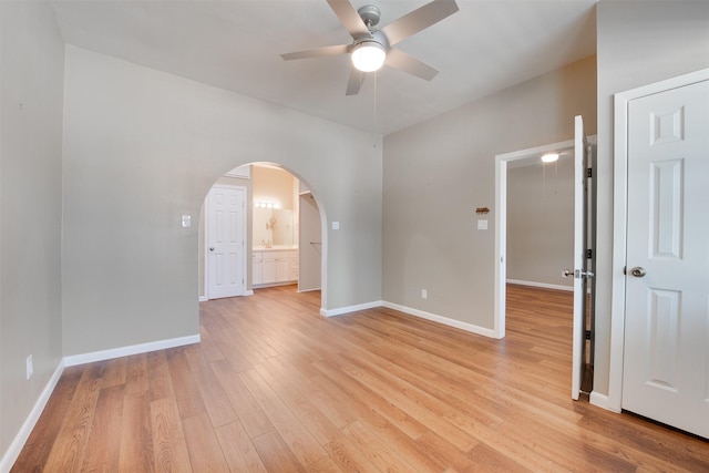 empty room featuring arched walkways, ceiling fan, light wood-style flooring, and baseboards