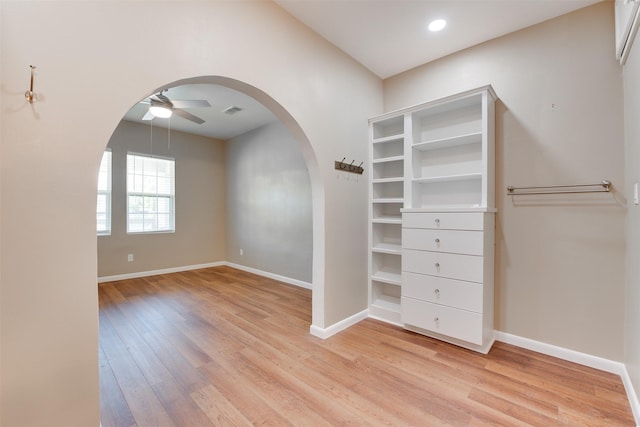 spacious closet featuring arched walkways, light wood finished floors, visible vents, and a ceiling fan