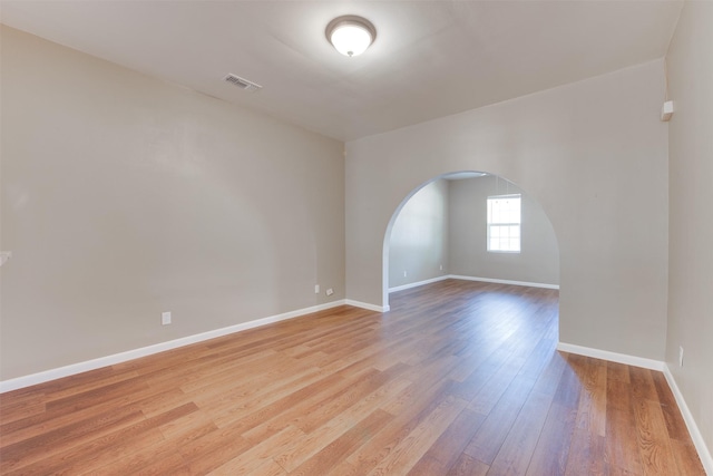 spare room with arched walkways, light wood-style flooring, visible vents, and baseboards