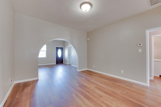 empty room with arched walkways, baseboards, visible vents, and light wood-style floors