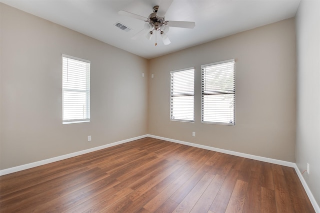 empty room featuring wood-type flooring, visible vents, ceiling fan, and baseboards