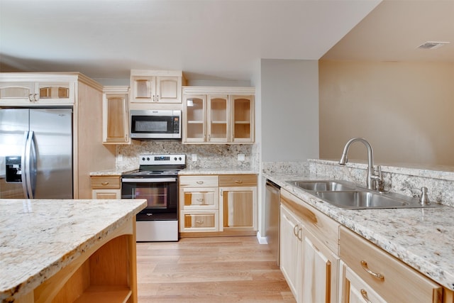 kitchen featuring stainless steel appliances, light wood-style flooring, glass insert cabinets, light brown cabinets, and a sink