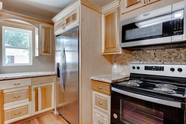 kitchen with light stone counters, light brown cabinets, light wood-style flooring, appliances with stainless steel finishes, and decorative backsplash