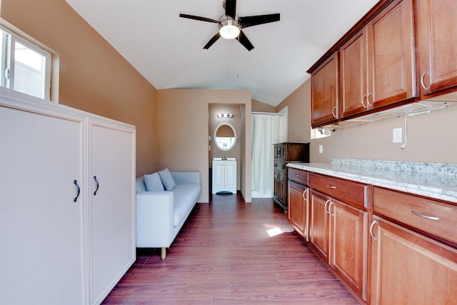 kitchen featuring ceiling fan, light stone counters, light wood-style floors, vaulted ceiling, and brown cabinetry