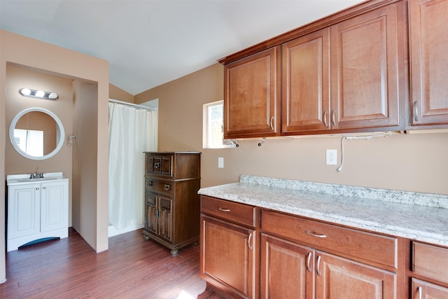 kitchen featuring a sink, light stone counters, wood finished floors, and brown cabinets