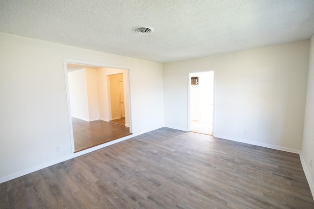 spare room featuring visible vents, a textured ceiling, baseboards, and wood finished floors