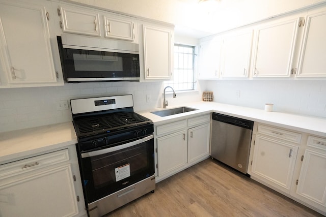 kitchen with tasteful backsplash, appliances with stainless steel finishes, light wood-style floors, white cabinetry, and a sink