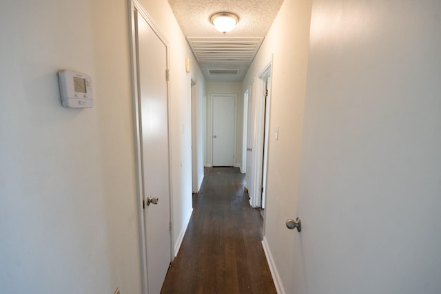 corridor featuring a textured ceiling, dark wood finished floors, visible vents, and baseboards