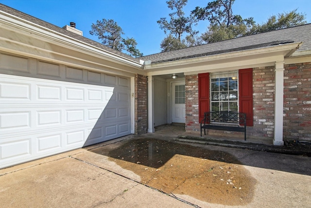 entrance to property with a garage, concrete driveway, brick siding, and roof with shingles