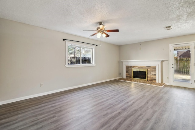 unfurnished living room with wood finished floors, a glass covered fireplace, visible vents, and a ceiling fan