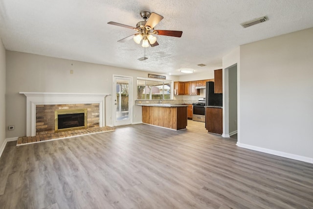 kitchen with brown cabinetry, stainless steel range with gas cooktop, open floor plan, and wood finished floors