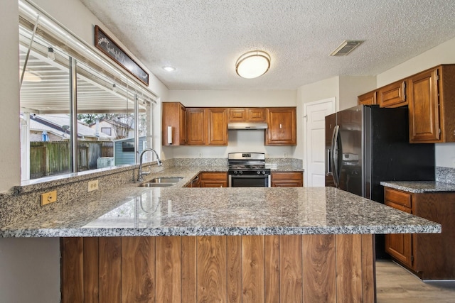 kitchen featuring under cabinet range hood, a peninsula, a sink, black fridge, and stainless steel range with gas stovetop