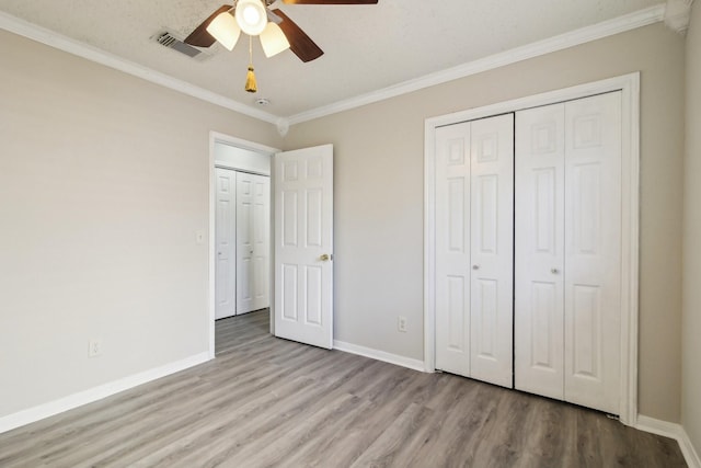 unfurnished bedroom featuring crown molding, visible vents, a ceiling fan, wood finished floors, and baseboards