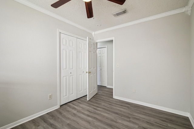 unfurnished bedroom featuring baseboards, visible vents, wood finished floors, crown molding, and a textured ceiling