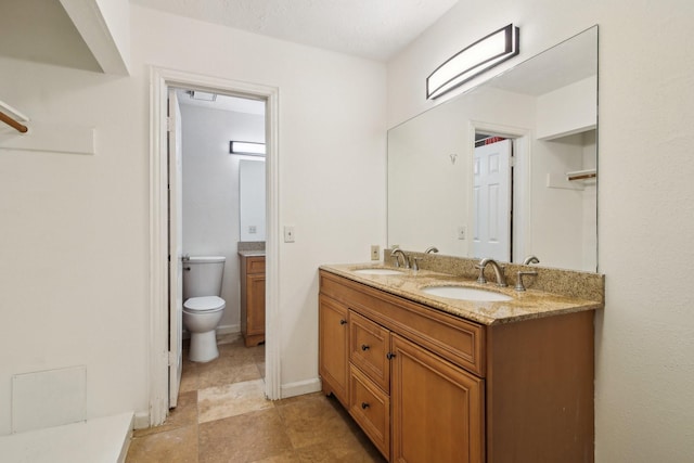 bathroom with baseboards, a sink, toilet, and double vanity