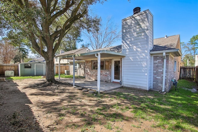 rear view of house featuring an outbuilding, a chimney, a storage shed, a patio area, and a fenced backyard