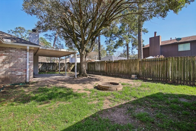 view of yard featuring a fire pit, an attached carport, and a fenced backyard