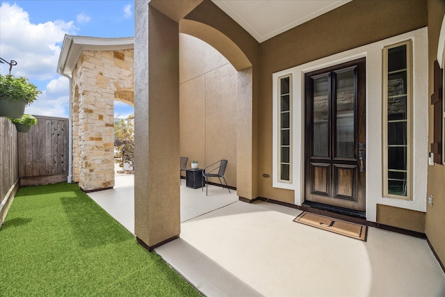 entrance to property featuring a patio, stone siding, fence, and stucco siding