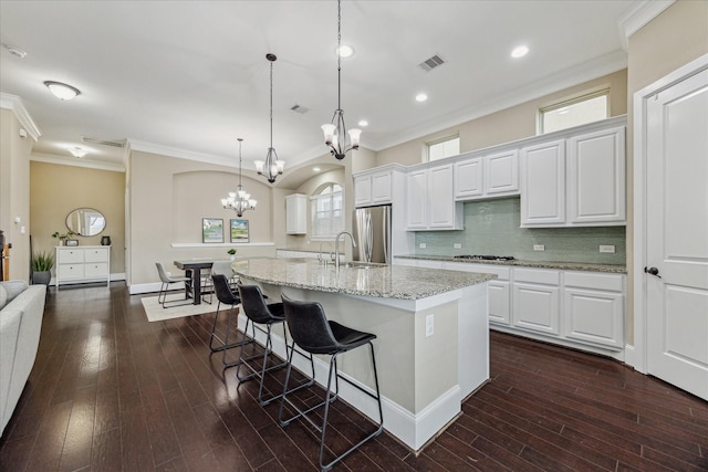 kitchen with a chandelier, a kitchen island with sink, dark wood-style flooring, freestanding refrigerator, and crown molding