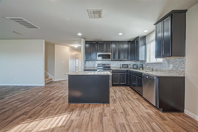 kitchen with appliances with stainless steel finishes, a center island, light wood-type flooring, and visible vents