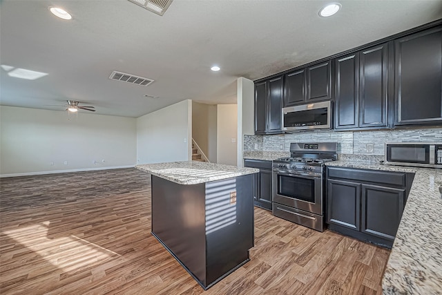 kitchen with visible vents, a kitchen island, stainless steel appliances, light wood-style floors, and backsplash