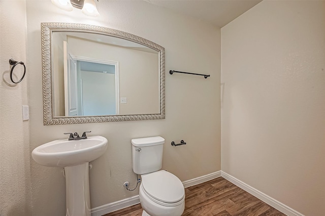 half bathroom featuring wood finished floors, toilet, and baseboards